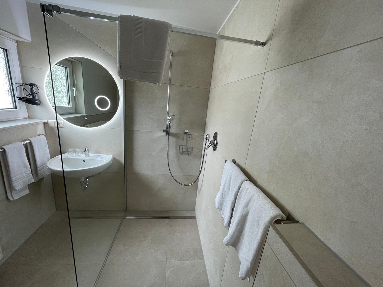 Salle de bains moderne au Landhaus Schend avec douche à l'italienne de plain-pied et miroir rond LED rétroéclairé